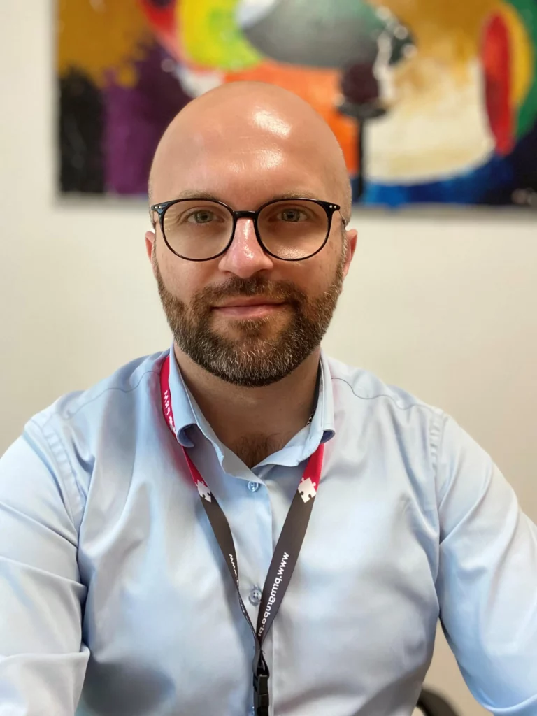 Foto von Bartosz Pachuta, Ihrem Kundenberater. Er lächelt und trägt ein elegantes Hemd.